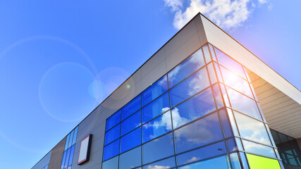 Fragment of a modern building made of steel and glass. Abstract modern commercial architecture fragment. Walls made of shiny glass and steel under blue sky.