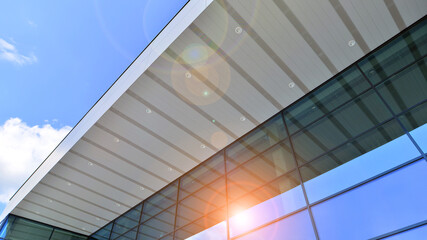 Fototapeta premium Fragment of a modern building made of steel and glass. Abstract modern commercial architecture fragment. Walls made of shiny glass and steel under blue sky.