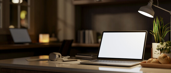 A laptop computer with a white-screen mockup on a table in a dark office at night.