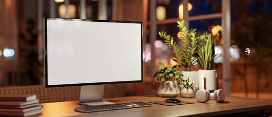 A computer with a white-screen mockup on a wooden table in a cozy room at night.