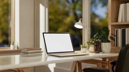 A laptop computer mockup and accessories on a white table by the window in a minimalist room.