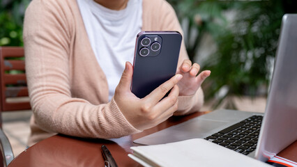A cropped image of a woman using her smartphone at a table outdoors, checking messages.