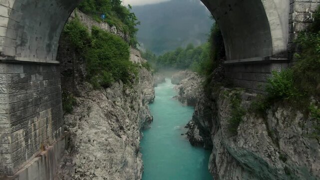 drone shot of the soca river in slovenia with blue water, a steet on the left site and trees around on a cloudy day