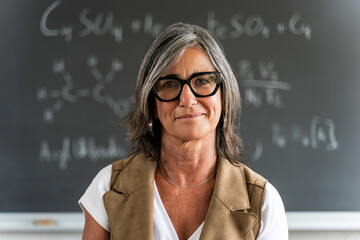 Mature female professor standing at college classroom looking at camera. Elegant School woman...