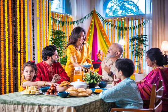 Portrait of happy Indian family in traditional outfit celebrating Diwali together at home eating food.