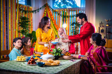 Portrait of happy Indian family in traditional outfit celebrating Diwali together at home eating food.