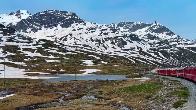Red Train Of Bernina Express On Railroad Track Passing By Lago Blanco In Graubunden, Switzerland. wide tracking shot