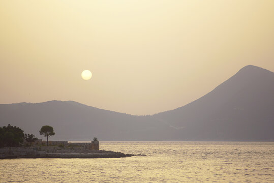 Evening seascape from Lustica: a piece of the island of Zanjice, the golden Adriatic Sea and the sun setting behind the mountains of the Croatian peninsula of Prevlaka. Summer holidays in Montenegro