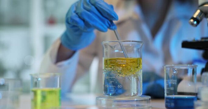 Scientist mixes yellow liquid in laboratory beaker