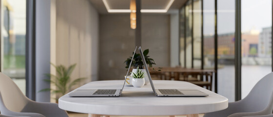 Two laptop computers on a modern white table in a contemporary meeting room or co-working space.