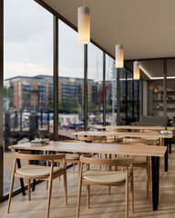 A contemporary restaurant or coffee shop features wooden tables by the window with a city view.