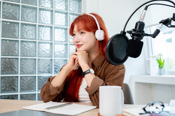 A beautiful Asian podcaster is in her studio, looking away and smiling with a dreamy expression.