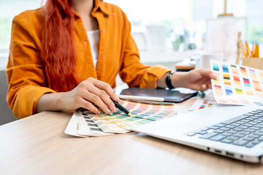 A female graphic designer working at her desk in the studio, selecting colors from a set of swatches