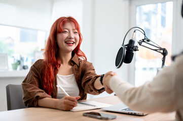 A friendly Asian female podcaster is shaking hands with a guest, greeting them to the podcast show.