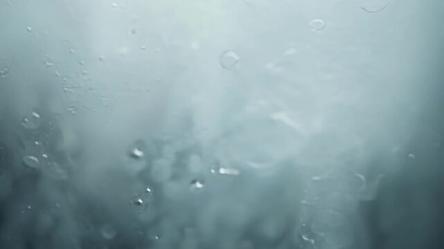 Water condensation forms on a glass surface, creating a visually appealing texture against a light background. The scene captures droplets and vapor, highlighting humidity and coolness