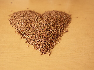 Pile of uncooked buckwheat in a heart shape on a wooden table surface. Popular Russian porridge and meal. Healthy grain. Organic product.