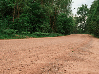 A dirt road with trees in the background. The road is empty and there is no one on it. Country side way without proper asphalt surface.