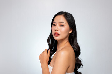 Gorgeous Asian woman poses against a grey background, showing her shoulder and looking at the camera