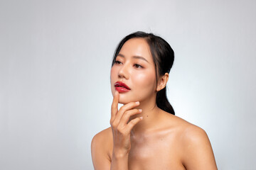 A beautiful Asian woman touches her chin while looking away, posing against a grey studio background