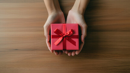 special moment where hands are presenting a beautifully wrapped red gift box adorned with a satin ribbon, emphasizing the warmth and thoughtfulness of giving, photo