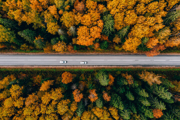 Aerial view of asphalt road with cars and colorful fall autumn forest in rural Finland.
