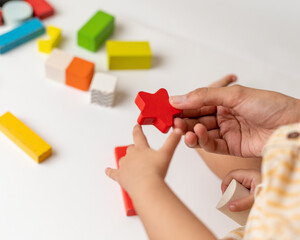 A mother helping little girl playing with multi colored wooden block toys, sitting on a white table, top shots