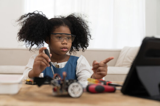 Girl student learning and building project toy robotics technology at home. African American child girl training and control toy robot in classroom