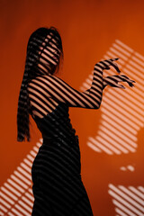 Brunette girl posing in a beam of light in the studio, on a red background, light and darkness.