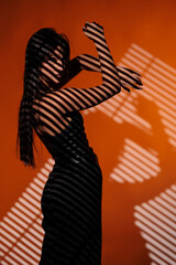 Brunette girl posing in a beam of light in the studio, on a red background, light and darkness.