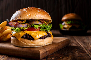 Close-up of a juicy cheeseburger with bacon, lettuce, tomato, onion, and melted cheese on a sesame bun, served on a wooden board with fries on the side, all set on a rustic wooden table.