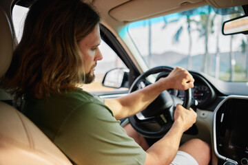 Naklejka premium A man driving a car with focus and determination on a sunny day, palm trees visible in the background, creating a relaxed yet intense atmosphere