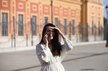 Fototapeta premium Young and beautiful Latin woman talking on mobile phone is having fun and is happy and smiling loudly. The woman is on the street and walks through the city. Concept communications.