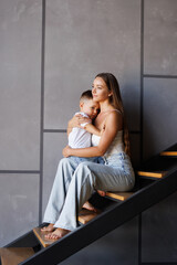 Young mother carrying small toddler son down the stairs indoors at home.