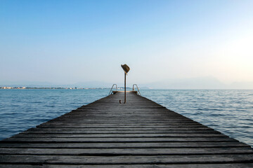 Un cappello su un bastone, piantato su un molo deserto che si estende nel Lago di Garda,...