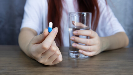 Medicine, Asian woman's hand holding white-blue pill capsule carefully with fingers and holding glass of water, symbolizing healthcare, Concept of pharmacy, medicine, supplement and medical treatment.