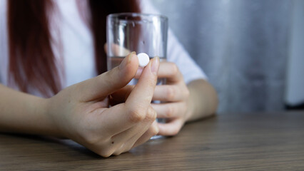 Medicine, Asian woman's hand holding white pills carefully with fingers and holding glass of water, symbolizing healthcare. Concept of pharmacy, medicine, supplement, vitamins and medical treatment.