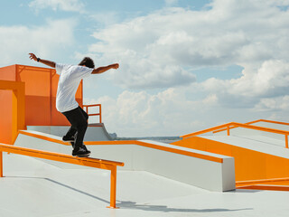 Latino Boy doing skateboard trick on rail in skatepark. Professional sportsman grinding on skateboard in outdoor park. Faceless unrecognizable young Latin skater doing Manual Grind trick on skate