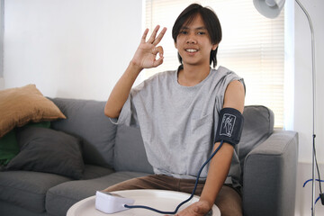 Young Asian Man Showing Ok Sign With Hands While Checking Blood Pressure Using Digital Technology
