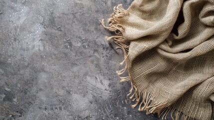 A textured beige fabric with frayed edges lays artfully against a rough, concrete surface, creating...