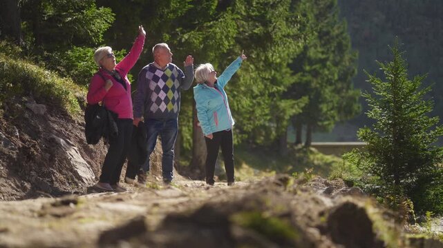 Two Senior Caucasian Women and a Man Exploring Nature Together and Waving to Someone Up. Concept of friendship, companionship, active aging, outdoor activity, well-being, retirement