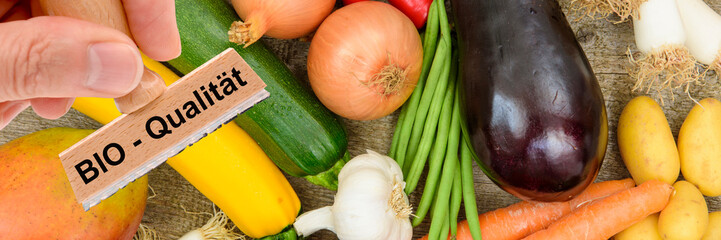 Ein Holzstempel ist beschriftet mit dem Aufdruck: Bio-Qualität über frischem Obst und Gemüse - FOTOMONTAGE