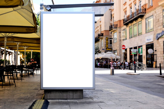 bus shelter at busstop. white poster ad display space and lightbox. mockup template. blank ad panel. glass design. urban street setting. soft background. silhouettes in a distance