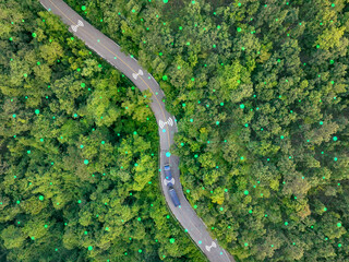 Aerial top view of driverless hydrogen-powered truck driving on highway through green forest. Sustainable transport. Autonomous vehicle. Green logistics. Zero-emission freight delivery. Clean energy.