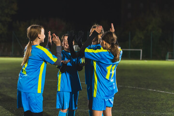 Obraz premium group of happy teenage football girls clapping each other while practicing football at night. High quality photo