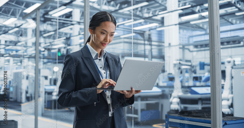Poster asian factory manager working on laptop at a futuristic industrial manufacture with autonomous robot
