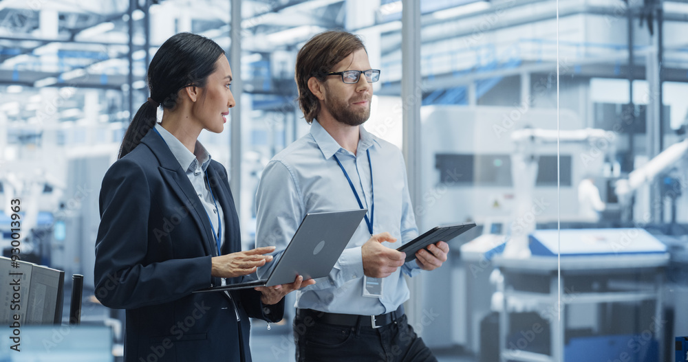 Aufkleber Factory Managers Using Computer Devices at Modern Manufacture with Autonomous Robot Hands. Female and Male Specialists Monitoring Technical Data, Analyzing Reports and Planning Updates