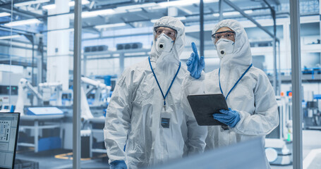 Industrial Scientists Wearing Disposable Protective Suits, Masks and Goggles at a Production Plant....