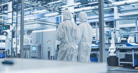 Sterile Modern Factory: Professionals in Coveralls Having a Conversation while Walking Through a...