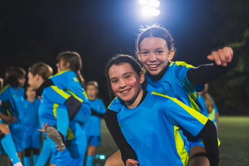 Teenage girls during training football. Team of laughing girls jumping on each others back, feeling joy and showing their fists and unity for victory. High quality photo