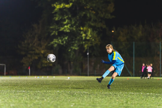 full shot of a little girl practicing in kicking a soccer ball at the practice, outdoors, late evening. High quality photo